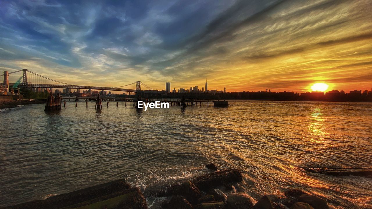 Scenic view of the east river and williamsburg bridge against sky during sunset