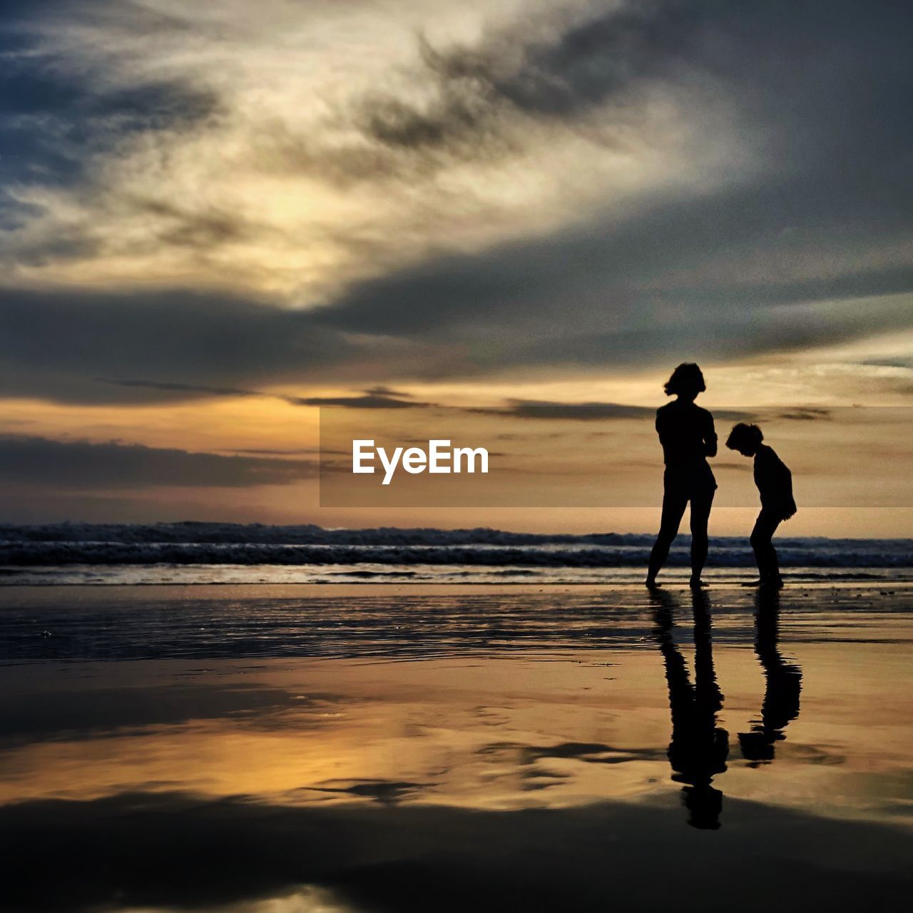 Silhouette people at beach against cloudy sky during sunset