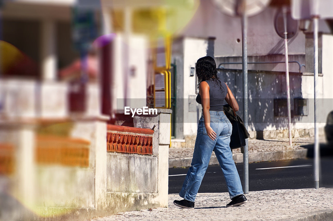 street, one person, road, adult, jeans, casual clothing, city, full length, architecture, young adult, clothing, women, standing, lifestyles, day, person, rear view, outdoors, city life, infrastructure, men, selective focus, business, denim, emotion, footwear, nature, urban area, store, spring