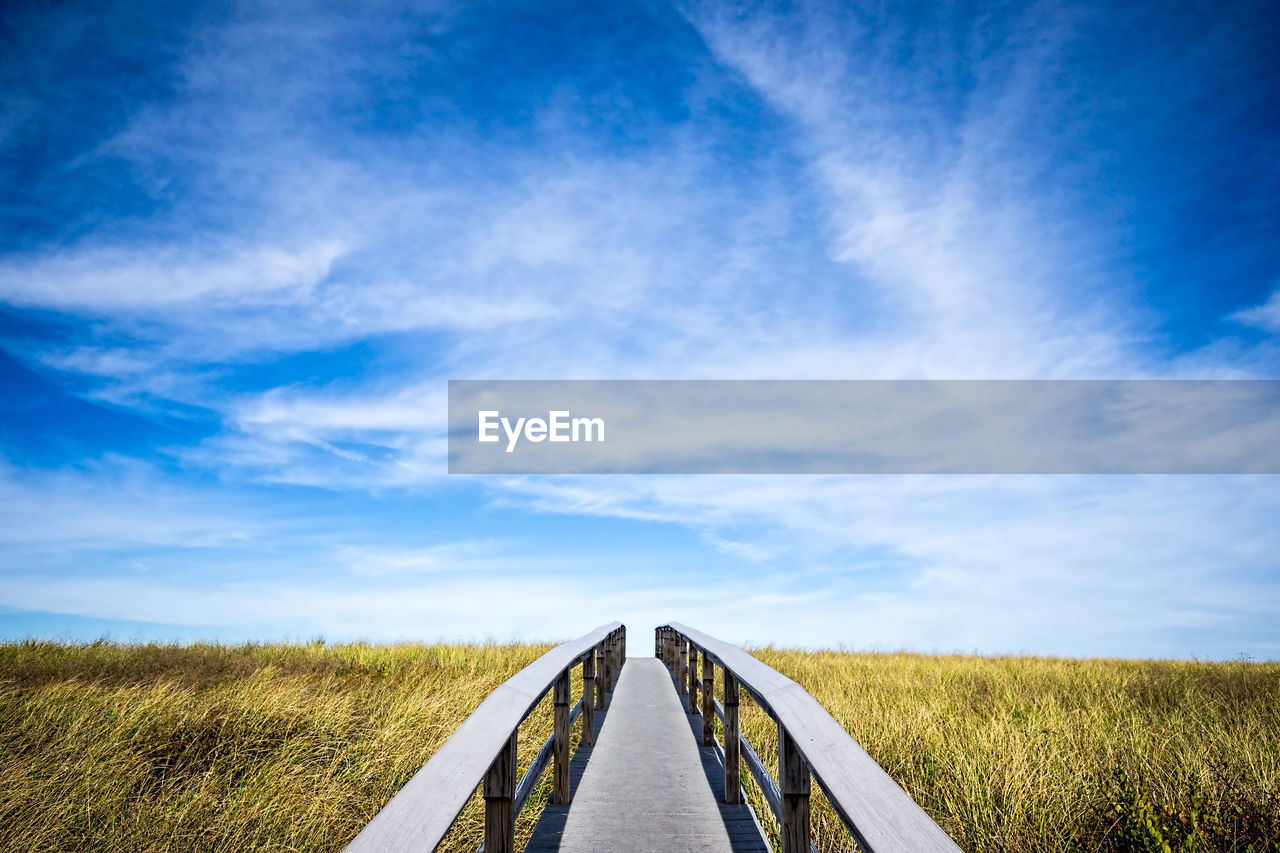 Footbridge over grassy field against sky