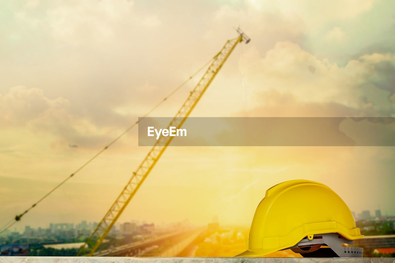 Crane and yellow helmet against sky during sunset