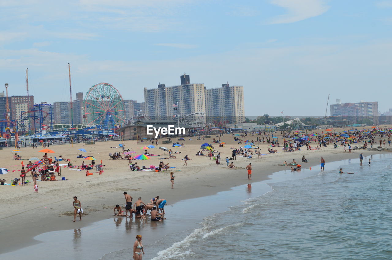 People at coney island beach against sky in brooklyn.