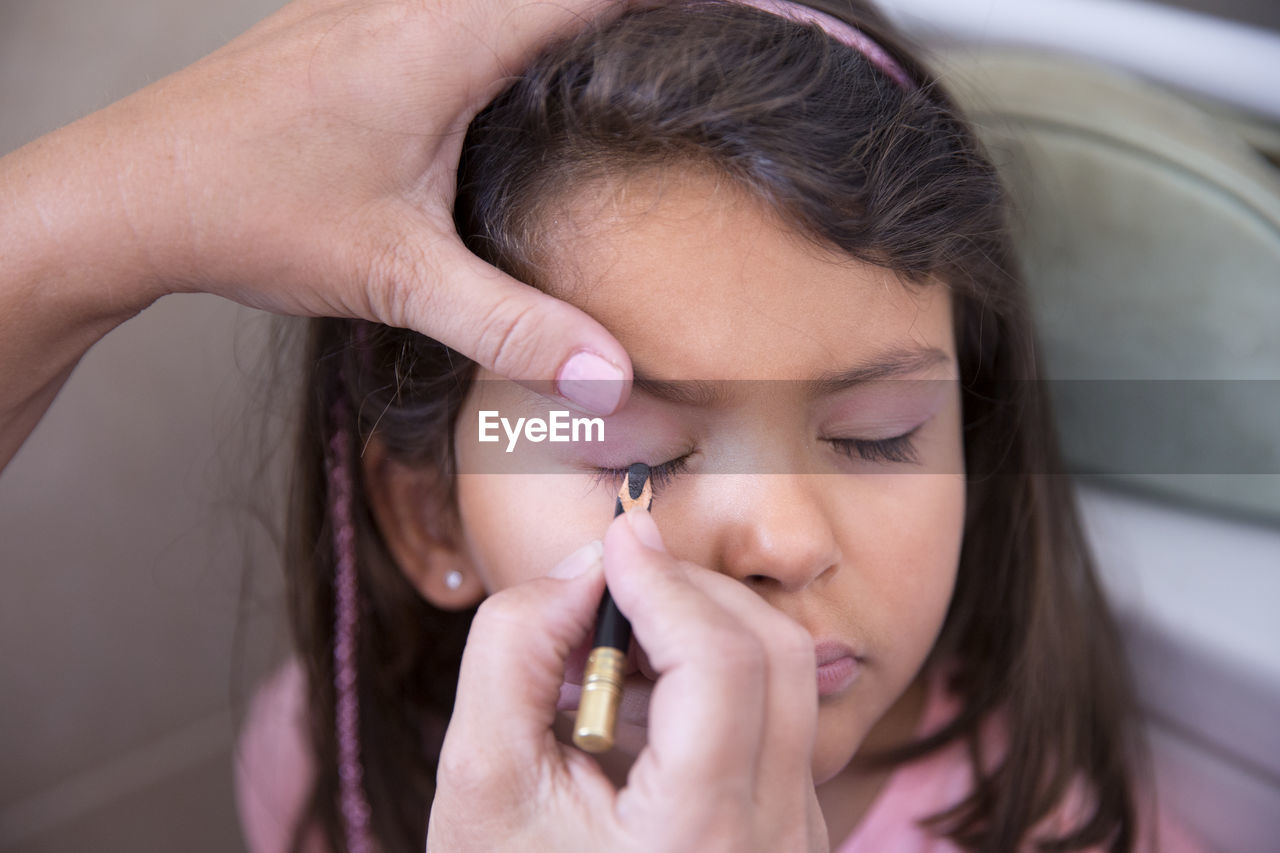 Cropped hands applying make-up to girl