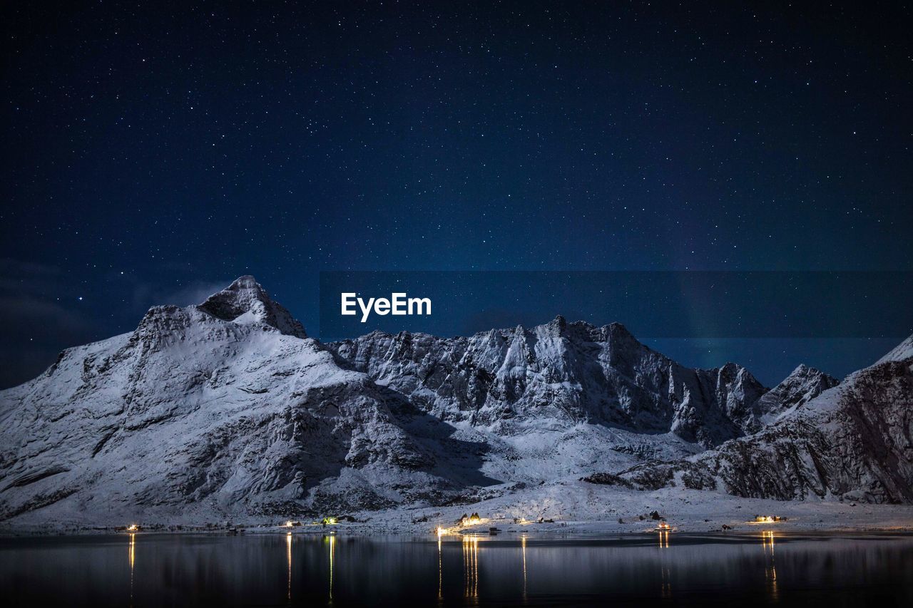 Scenic view of snowcapped mountains by lake against star field at night