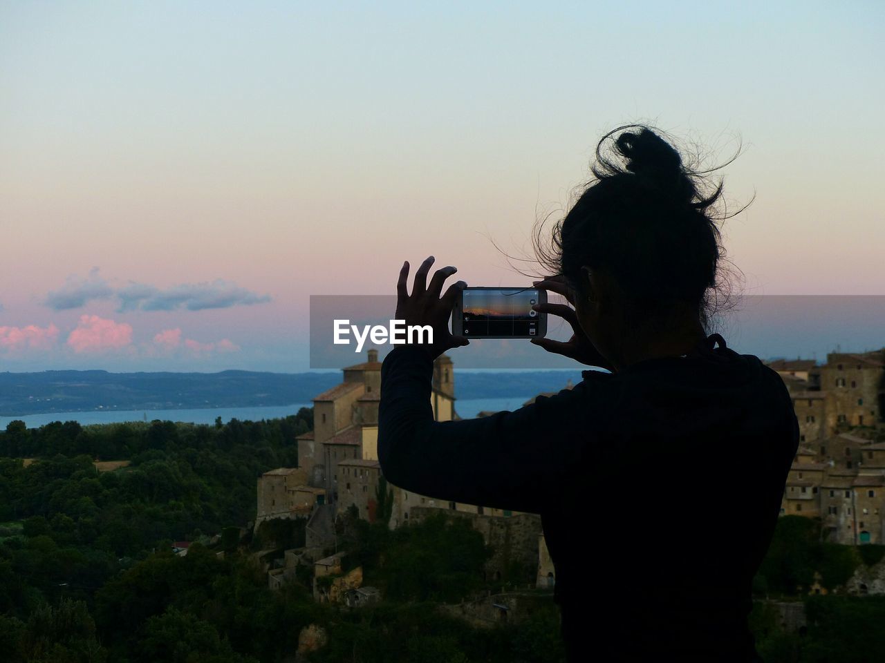 Silhouette woman photographing with smart phone against sky during sunset