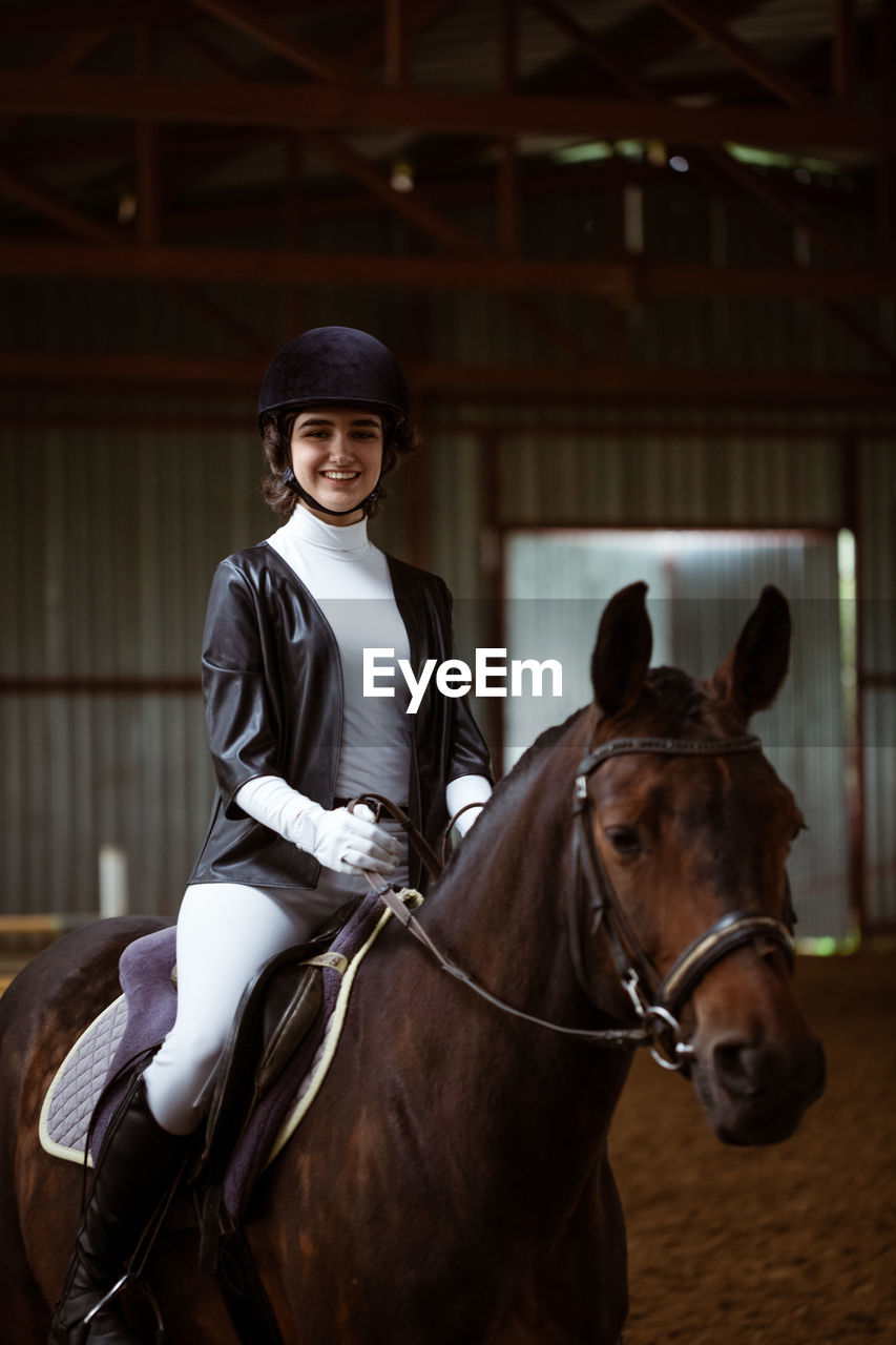 Portrait of smiling woman riding horse in stable