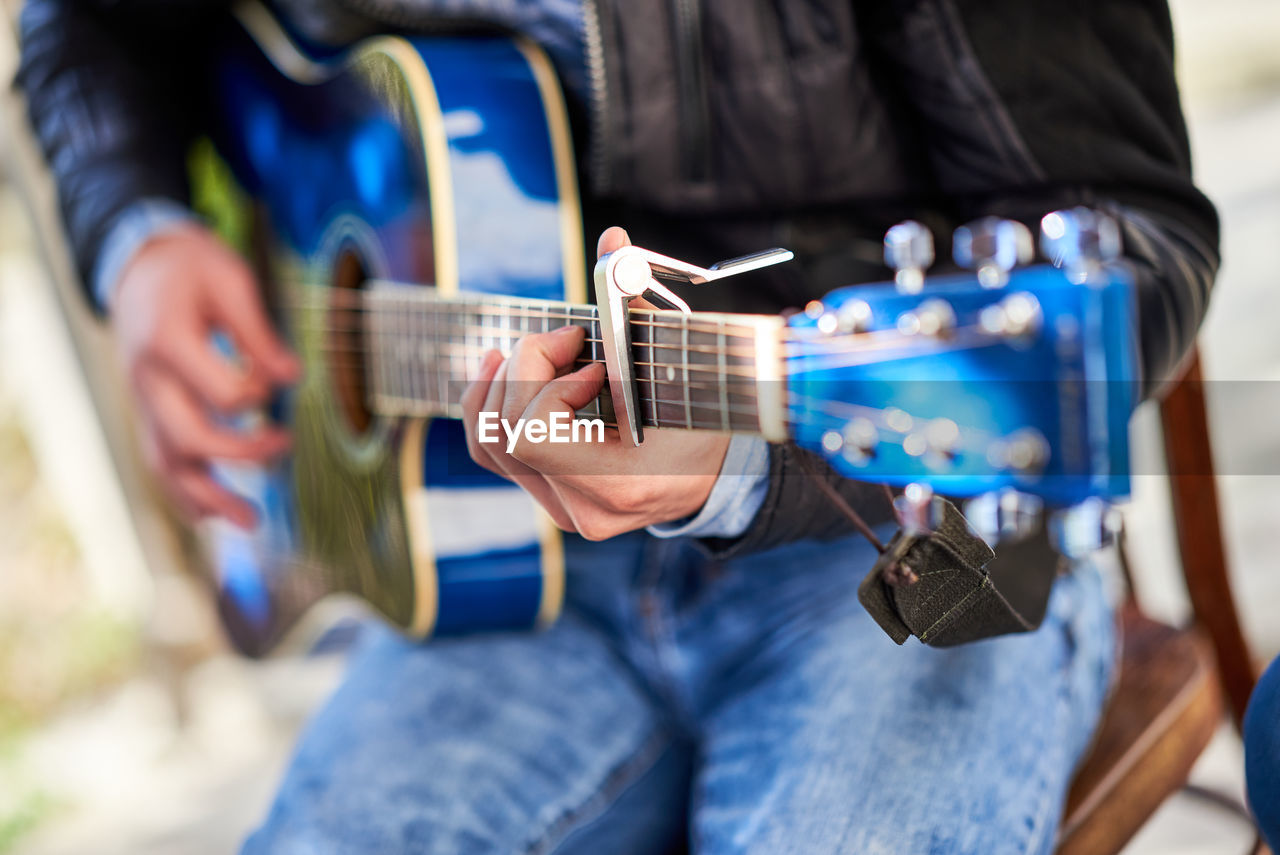 MIDSECTION OF MAN PLAYING GUITAR AT CAMERA