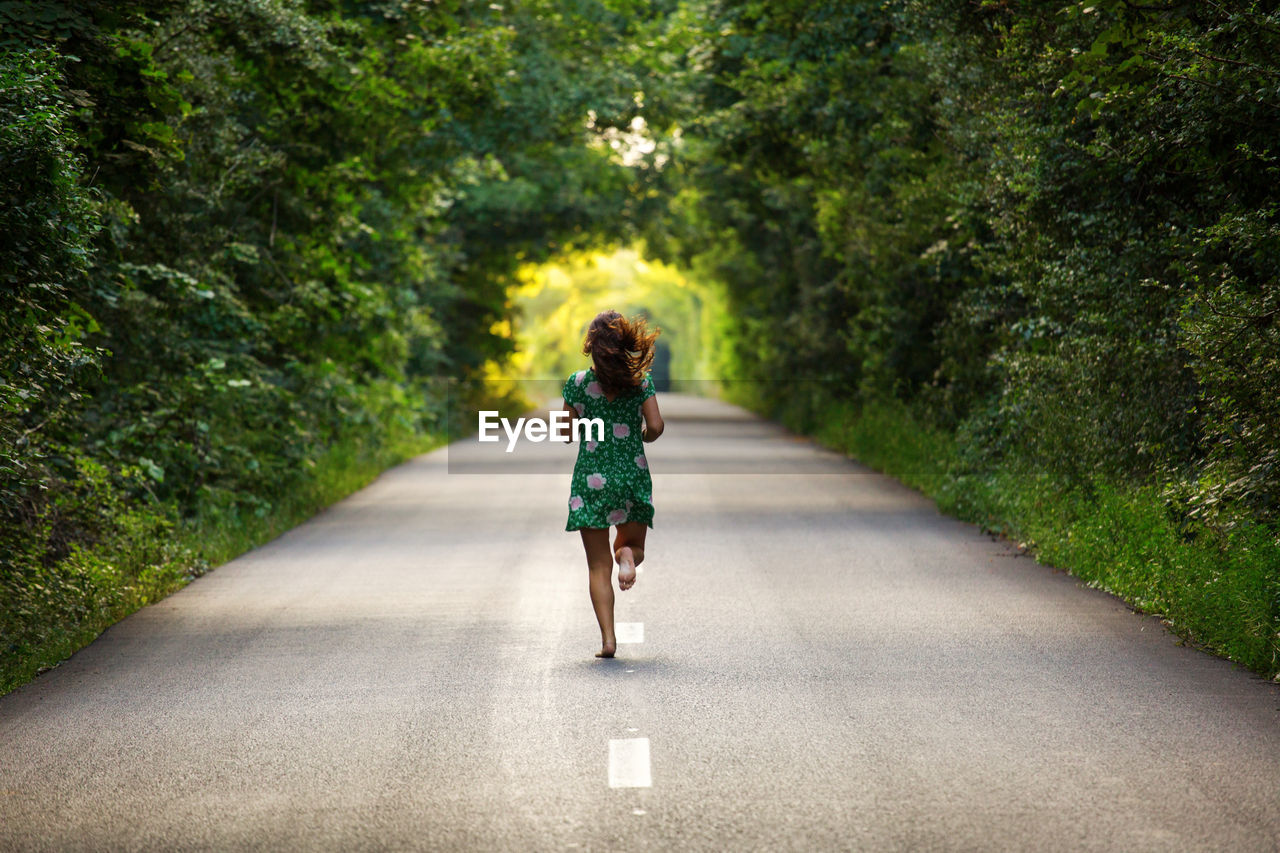 Rear view of woman running on road amidst trees