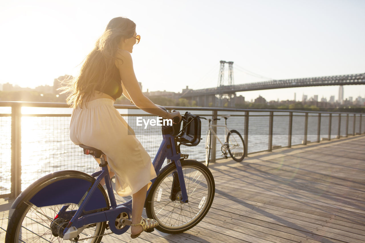 Happy woman riding bicycle on promenade during sunset