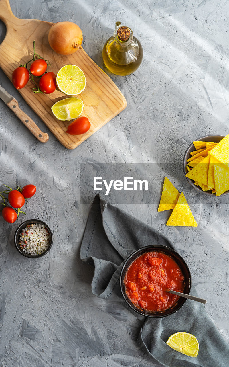 Tomato dip with with nachos tortillas and main ingredients on grey background. flat lay