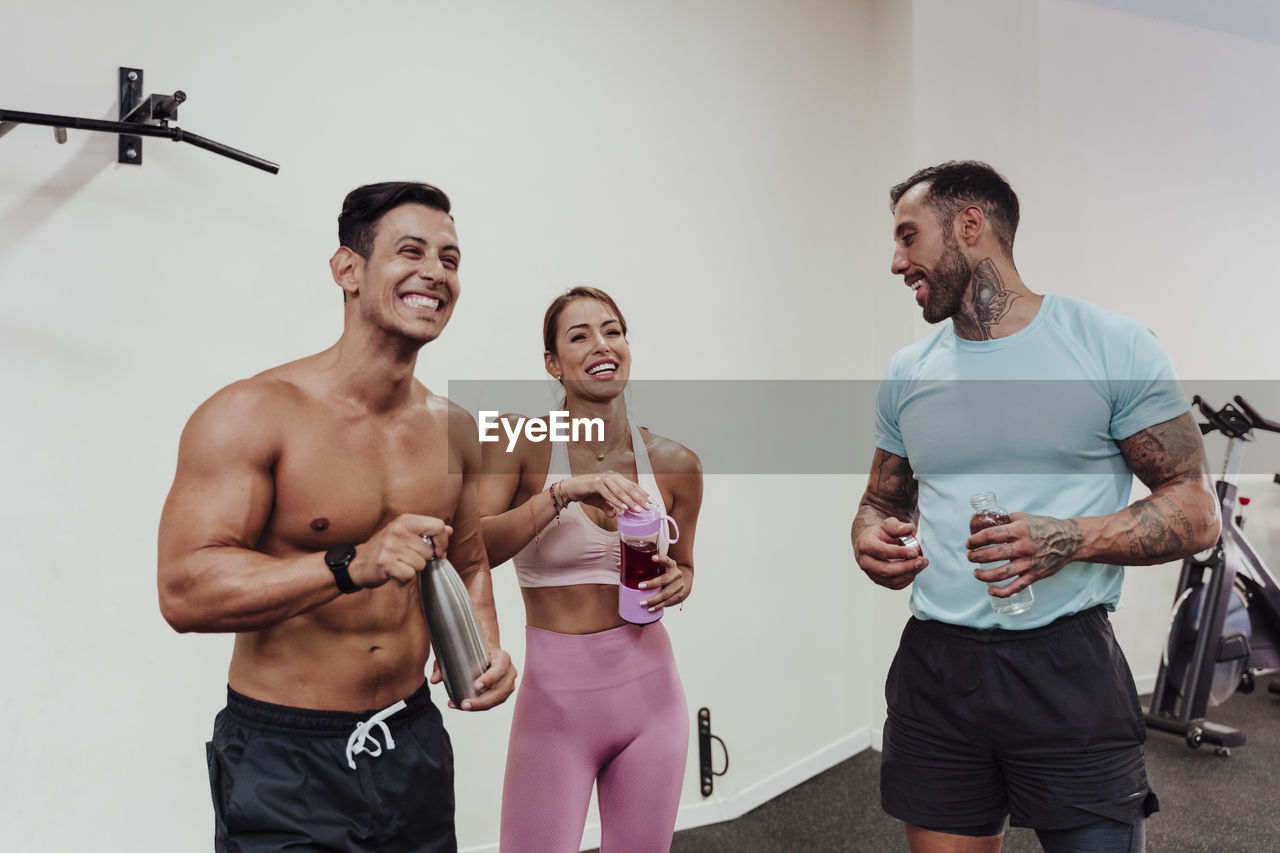 Cheerful sports people drinking water while standing at gym