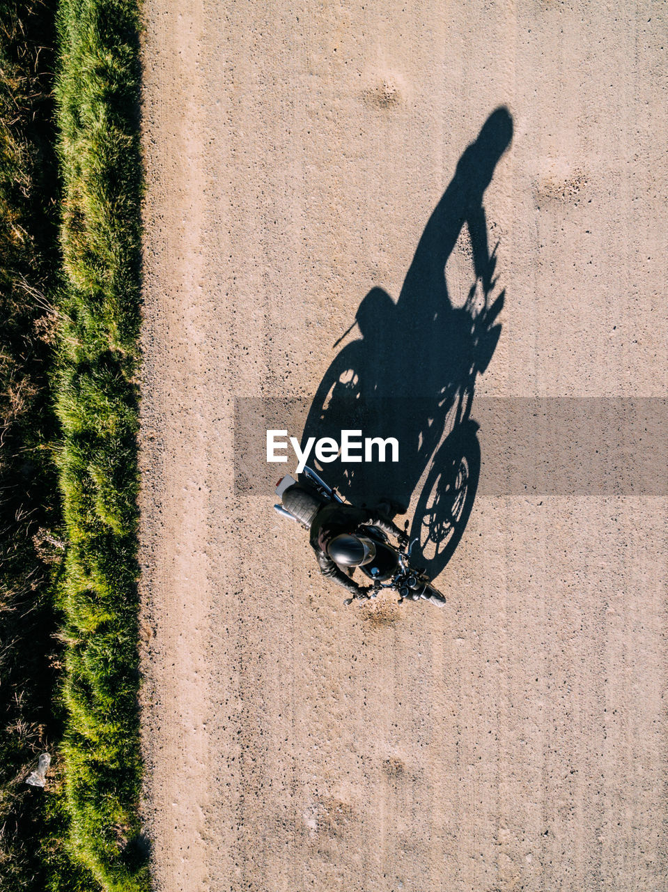 From above aerial view of person driving motorbike on rural road in sunlight in countryside