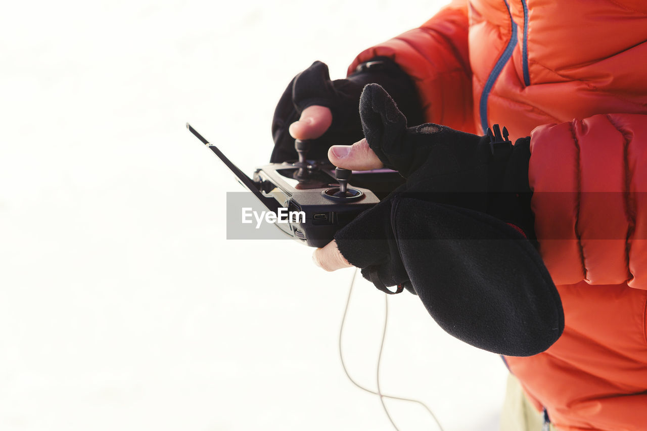 Midsection of man in warm clothing holding remote control against white background