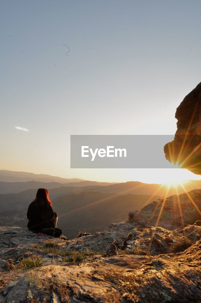 Rear view of woman sitting against mountains during sunset