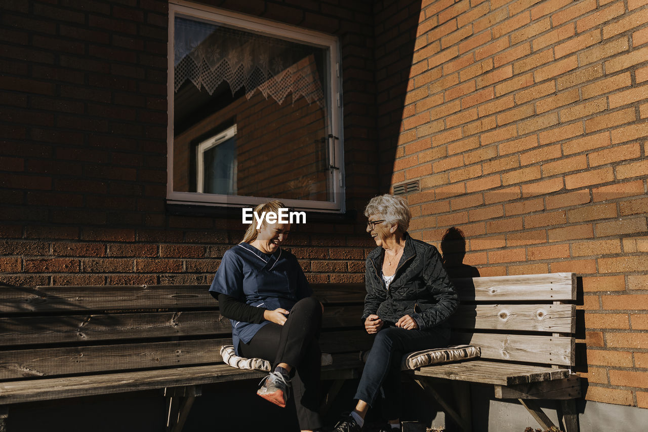 Home caretaker and senior woman sitting on bench and laughing