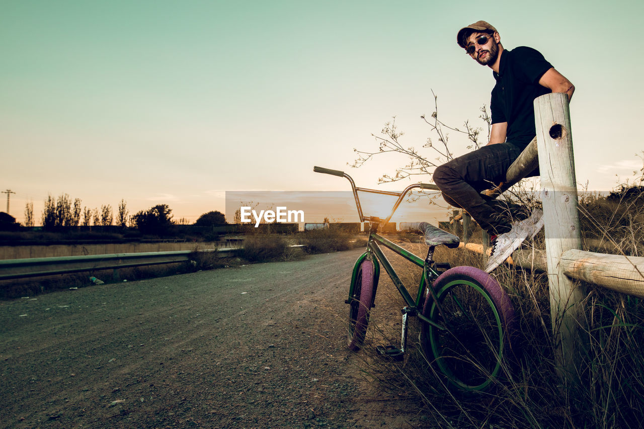 Side view portrait of man sitting with bicycle on road during sunset