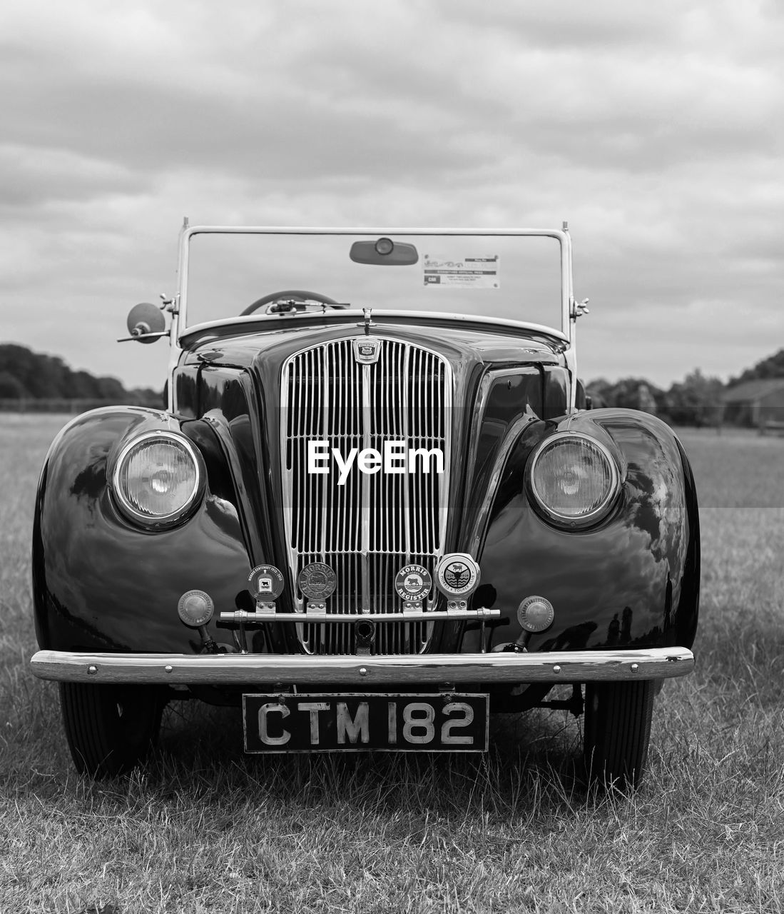 vehicle, car, land vehicle, vintage car, motor vehicle, retro styled, mode of transportation, black and white, transportation, cloud, sky, grass, antique car, nature, nostalgia, monochrome photography, field, luxury vehicle, plant, monochrome, automobile, land, day, landscape, front view, the past, headlight, history, no people, old, rural scene, outdoors, metal