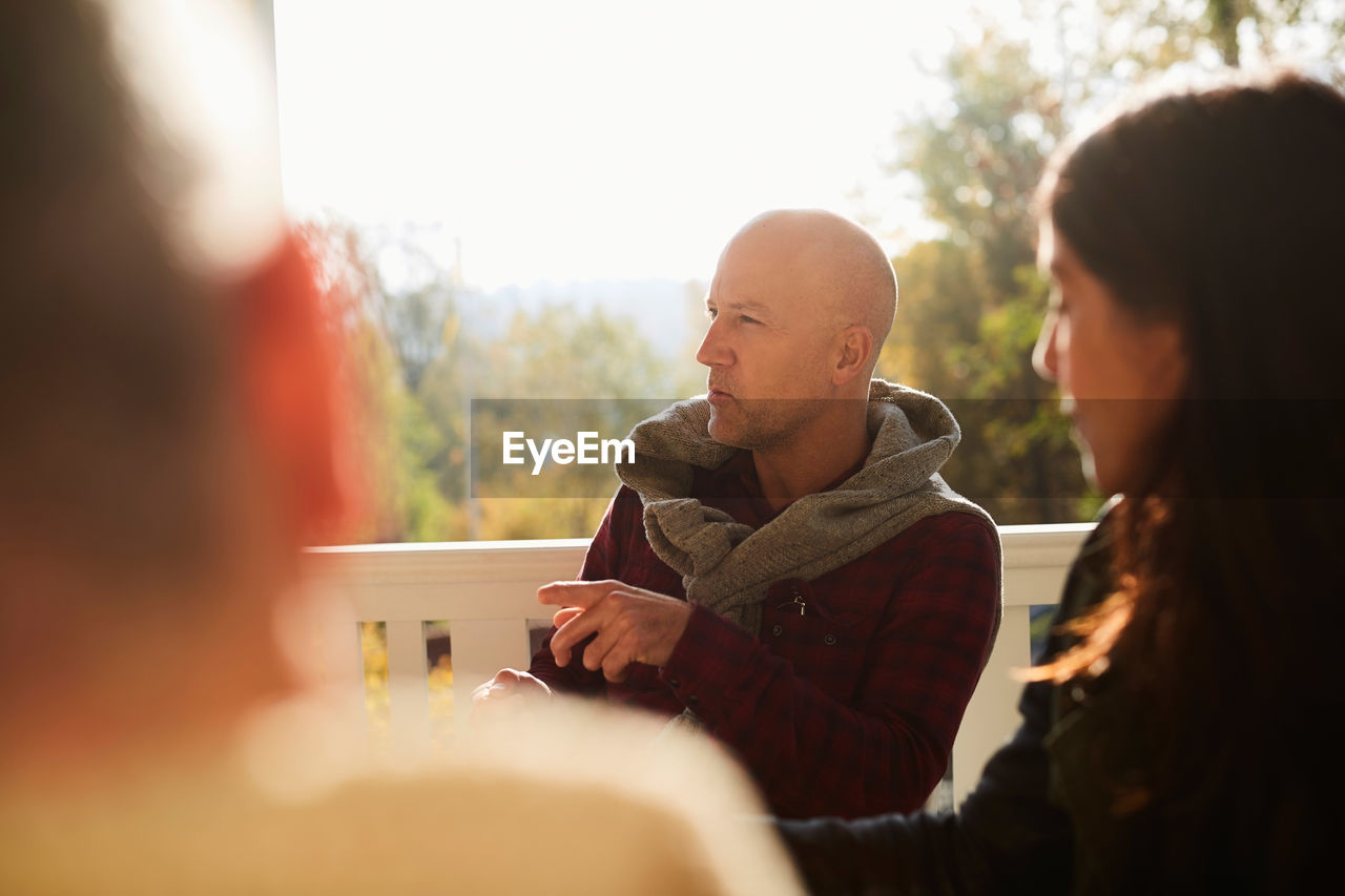 Mature friends talking while sitting on porch during sunny day