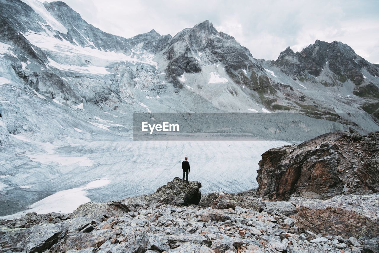 High angle view of man standing on rock formation in front of swiss alps