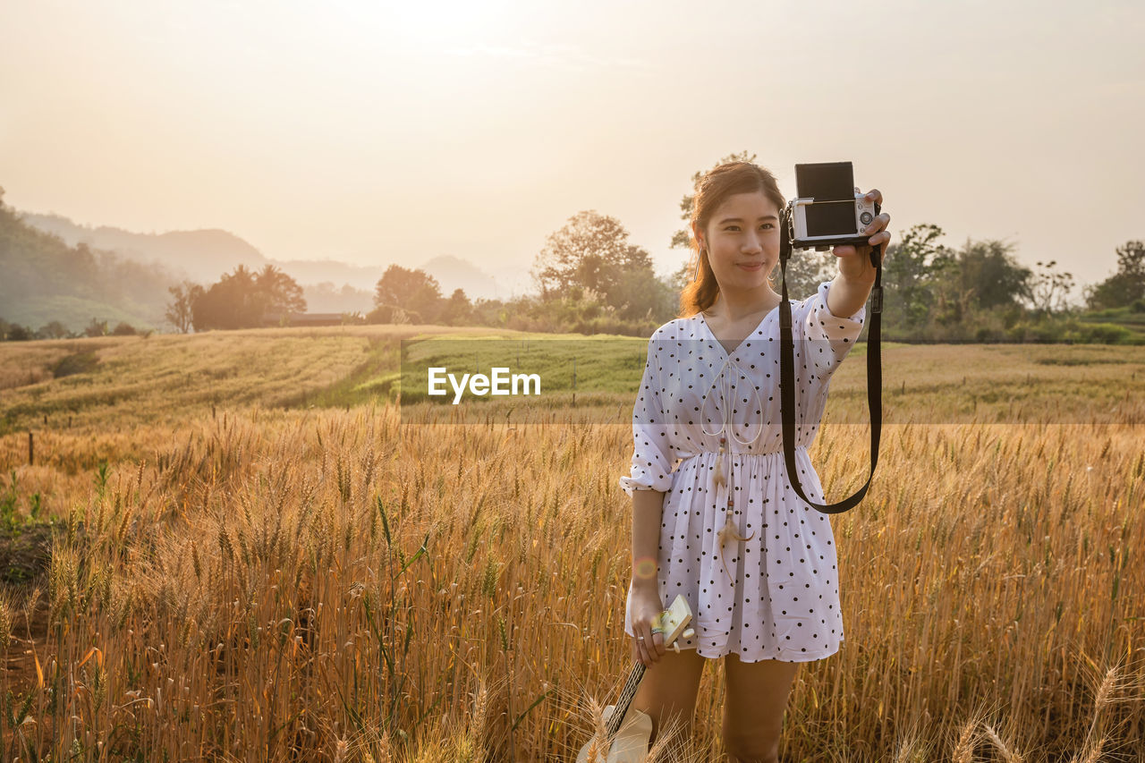 rear view of young woman photographing while standing on field