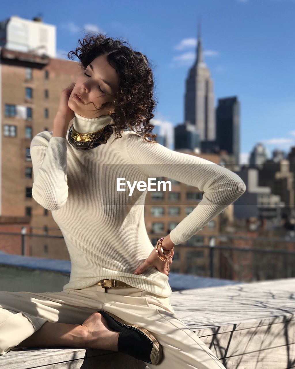 YOUNG WOMAN SMILING WHILE SITTING AGAINST BUILDINGS