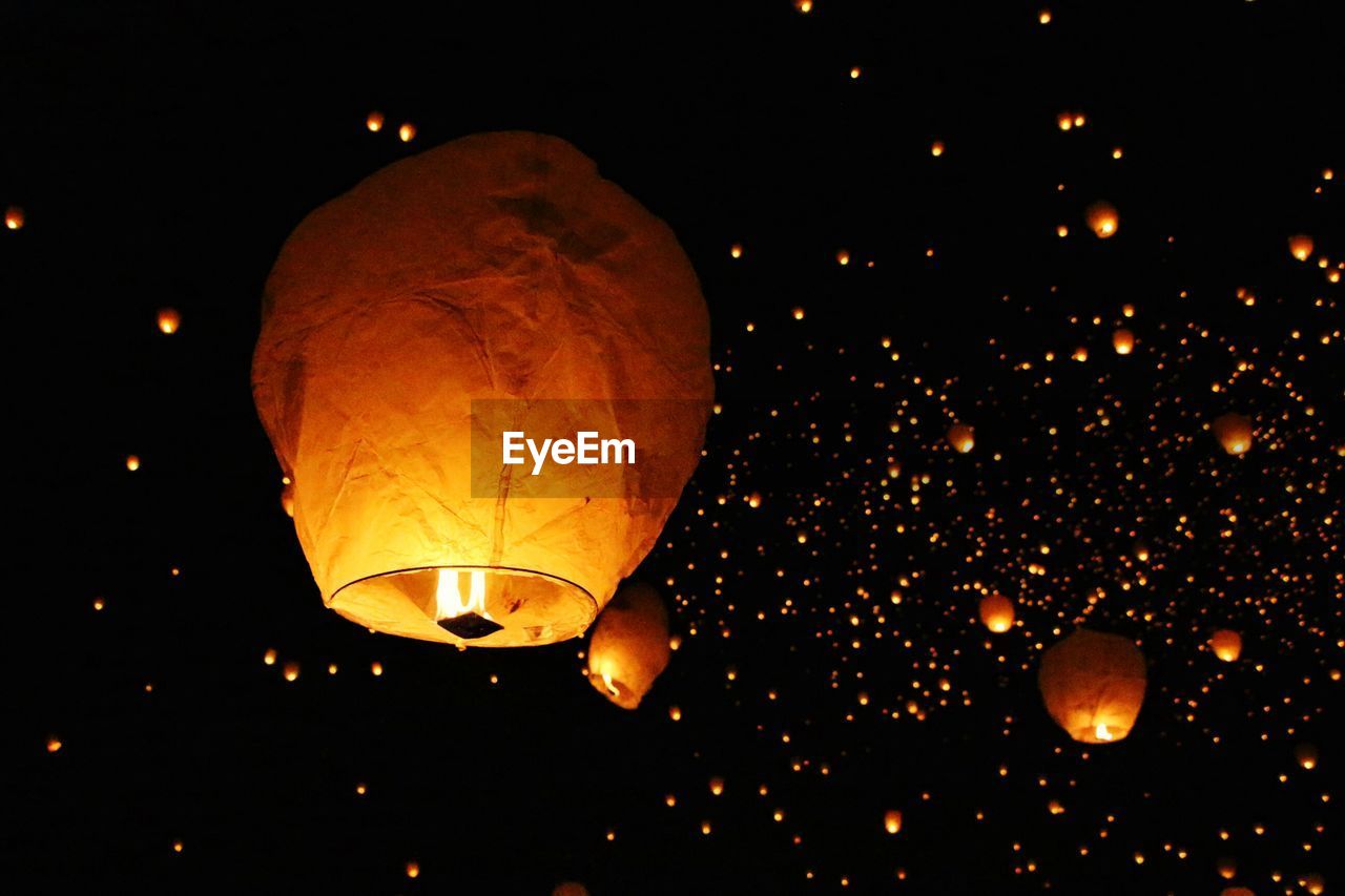 Low angle view of illuminated paper lanterns flying against sky at night