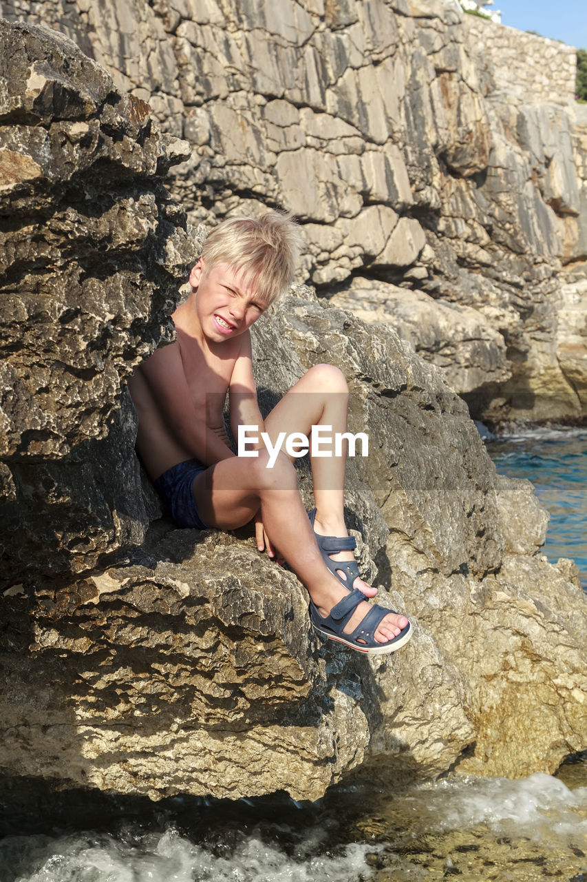 MIDSECTION OF WOMAN SITTING ON ROCK AGAINST ROCKS