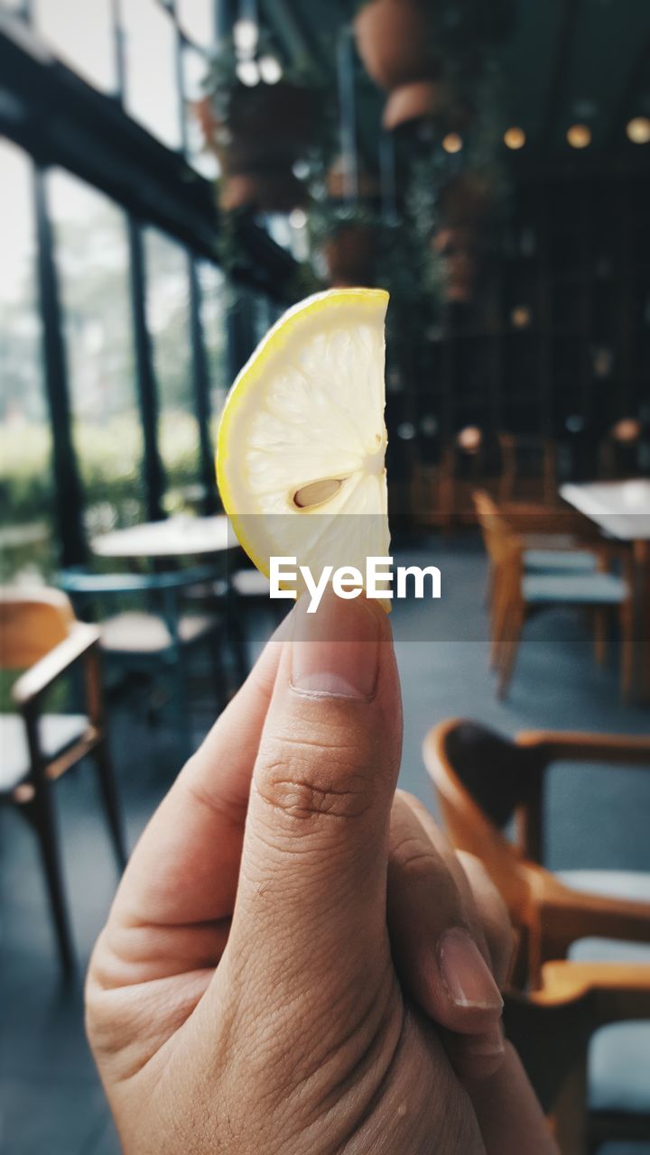 Cropped hand on woman holding sliced lemon in restaurant