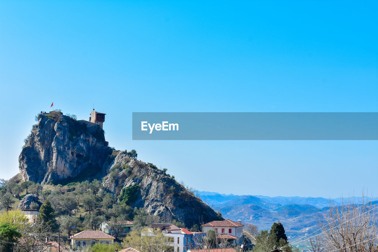 Buildings and mountains against clear blue sky