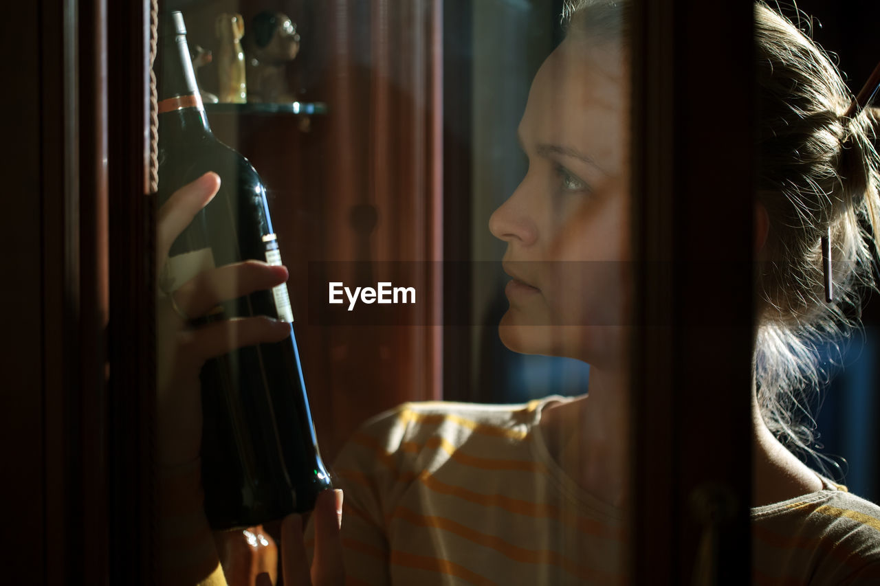 Young woman looking at wine bottle seen through glass