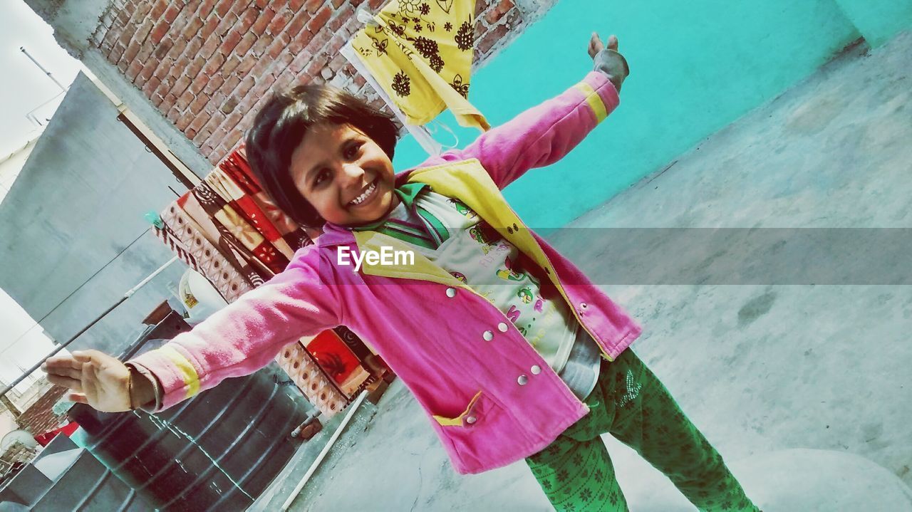 Portrait of cheerful girl with arms outstretched standing against wall