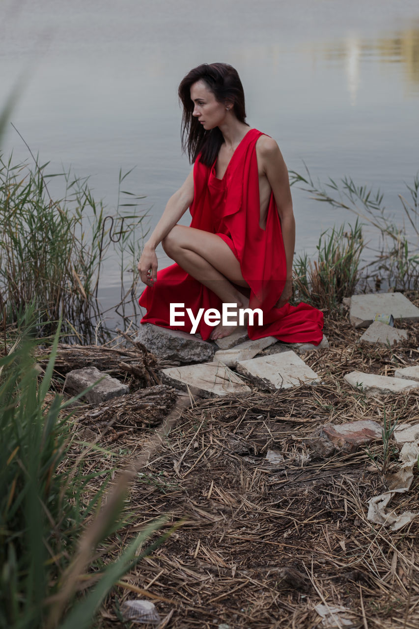 BEAUTIFUL YOUNG WOMAN SITTING ON LAND BY WATER