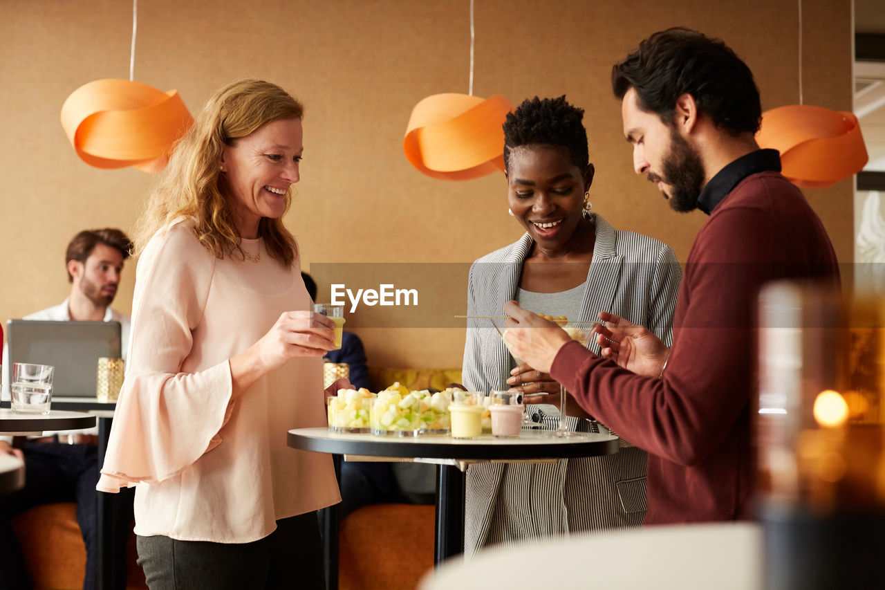 Businessman and smiling businesswomen with food standing by table at workplace