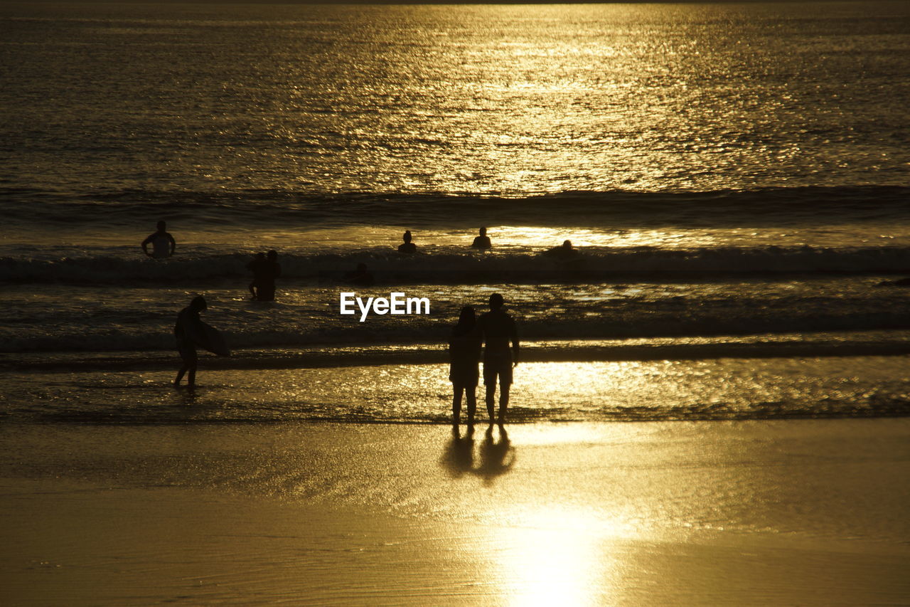 Silhouette people standing at beach during sunset