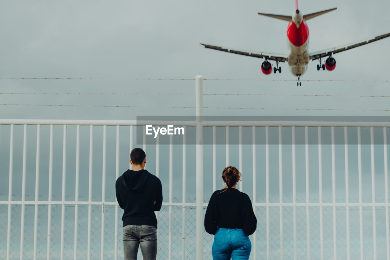 People looking at airplane flying against sky