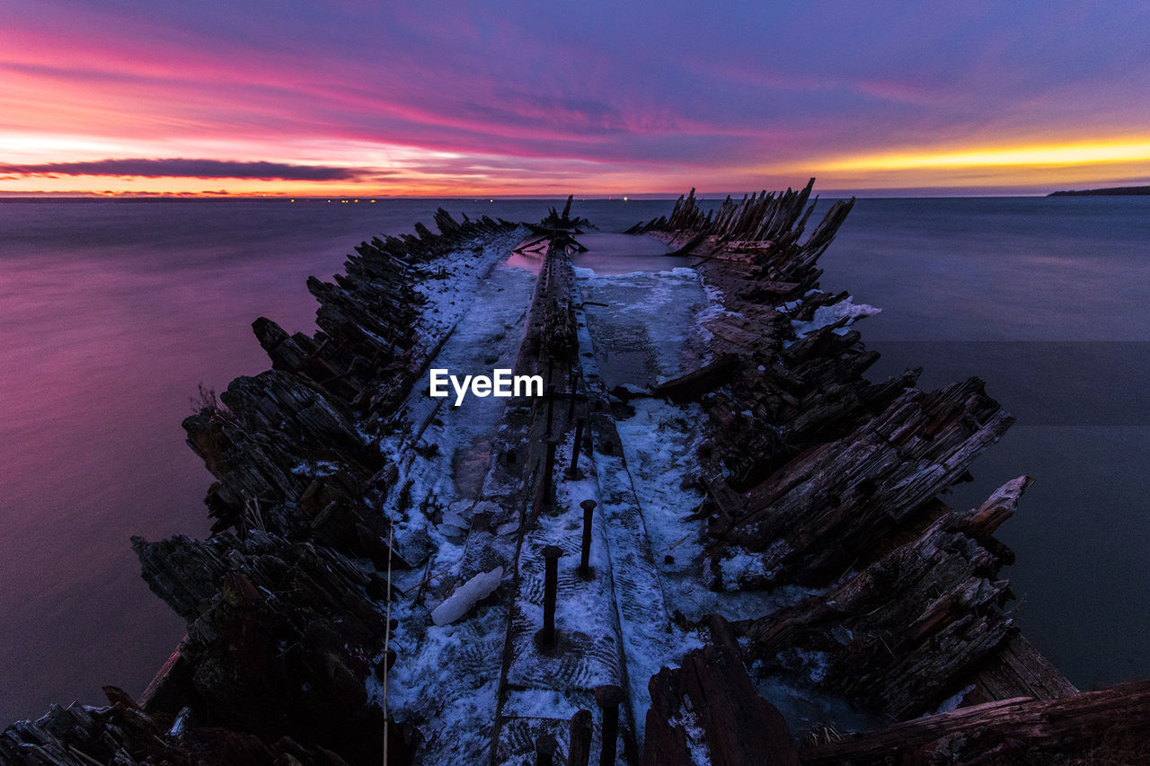 Shipwreck on sea against sky in winter during sunset