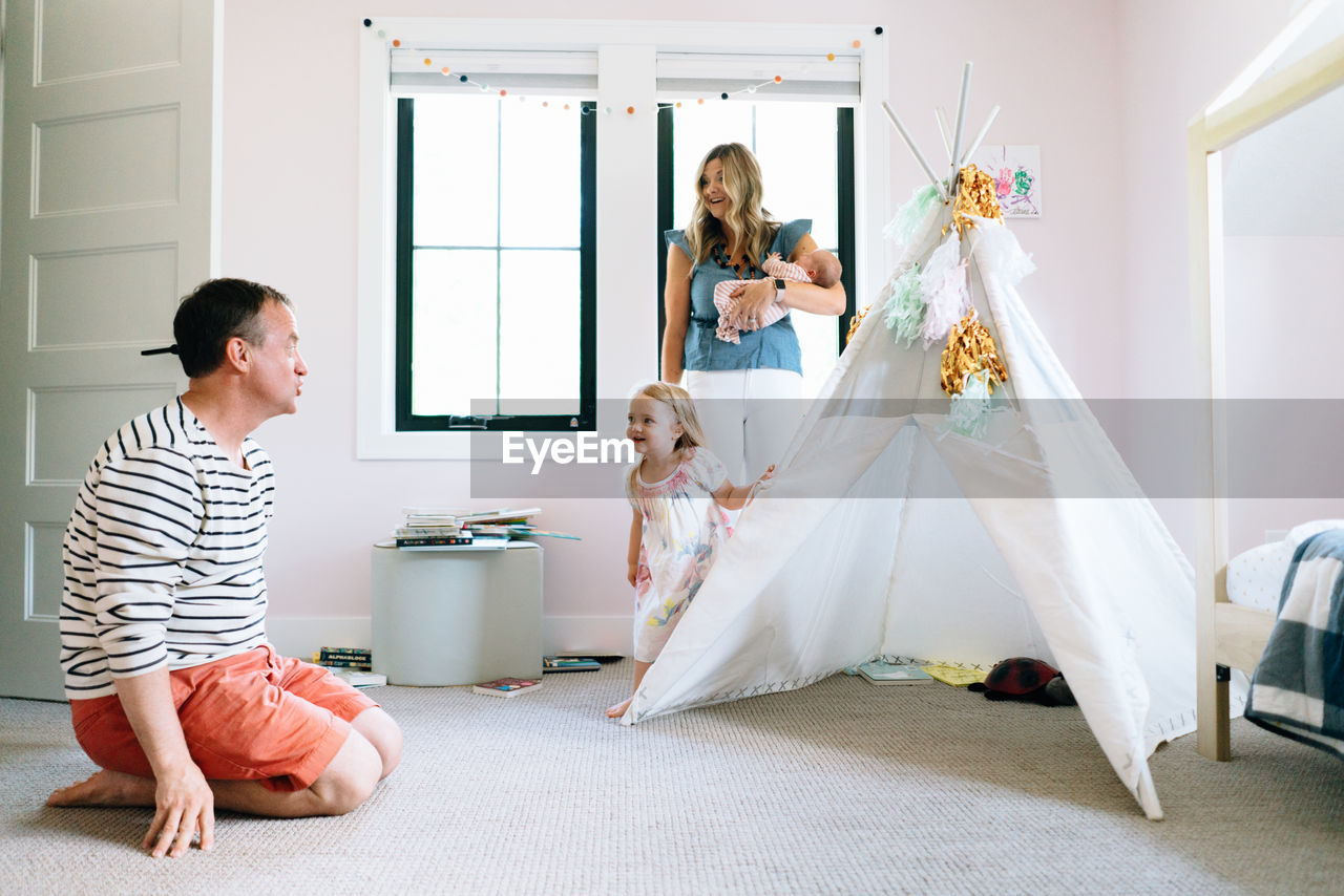 A family of four play together in a child's room with a modern tipi