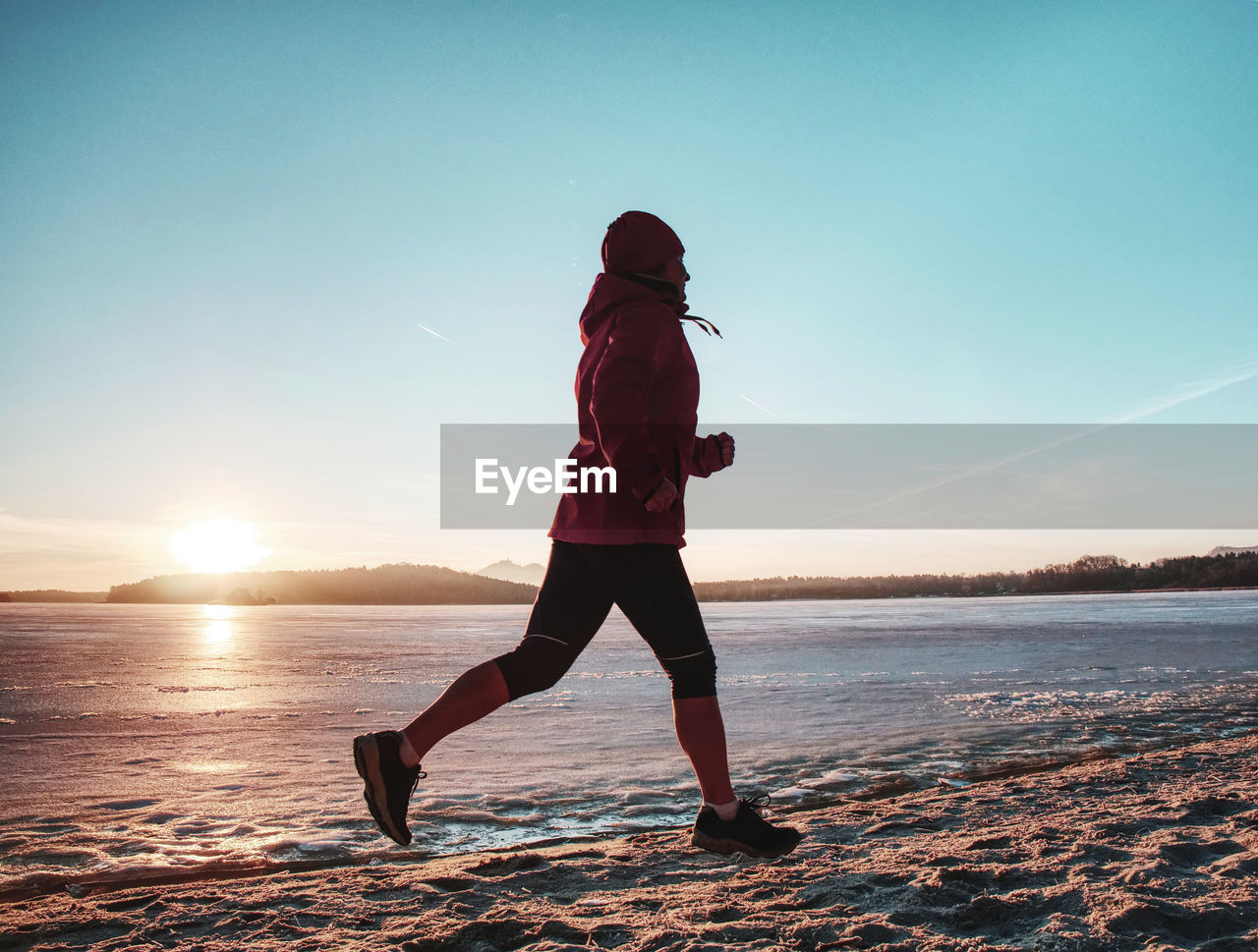 Running sport woman. female runner jogging at cold winter bay wearing warm sporty running clothing