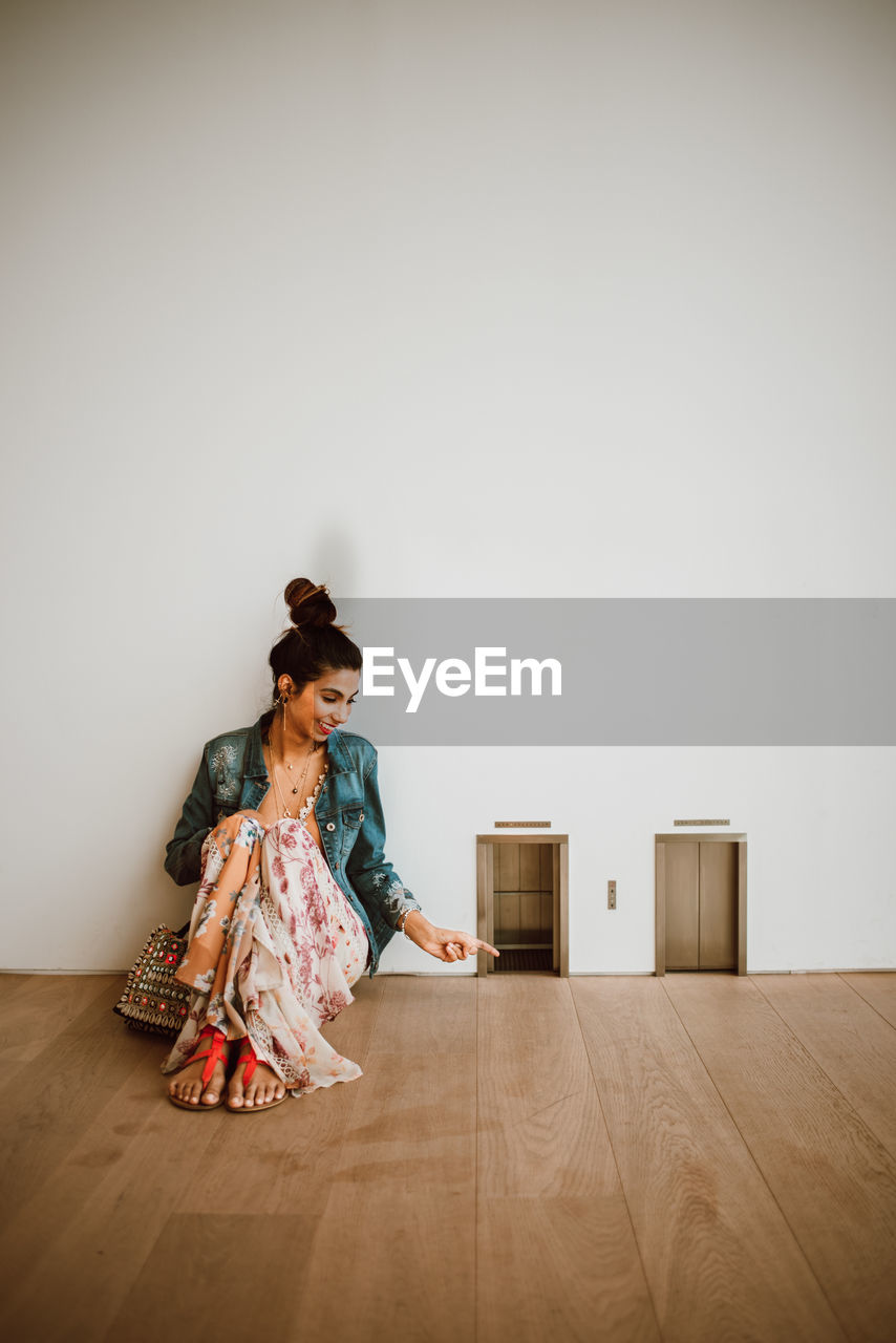 Woman sitting on hardwood floor against wall