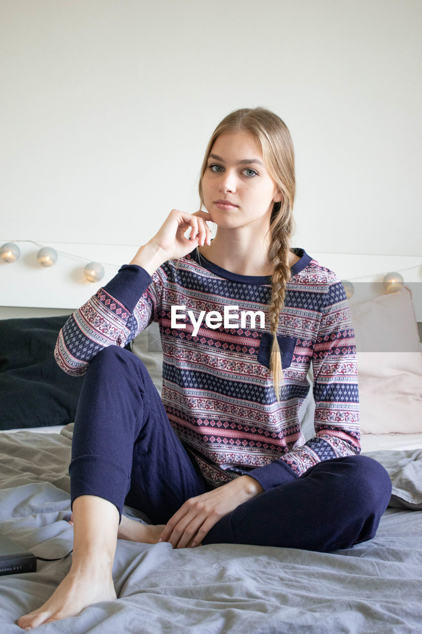 PORTRAIT OF YOUNG WOMAN SITTING ON BED