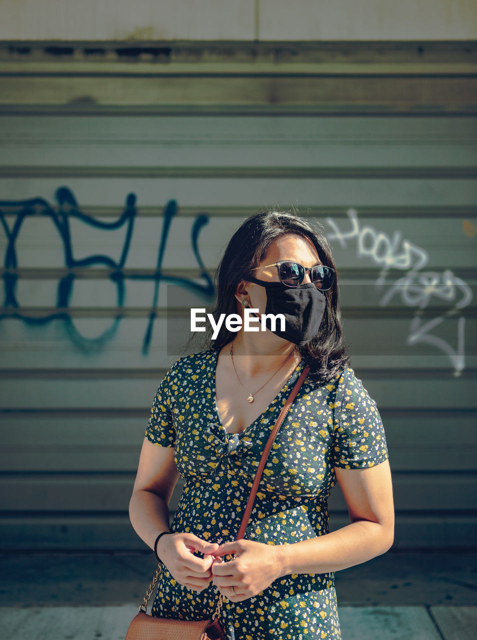 Young woman wearing sunglasses and mask while standing against wall