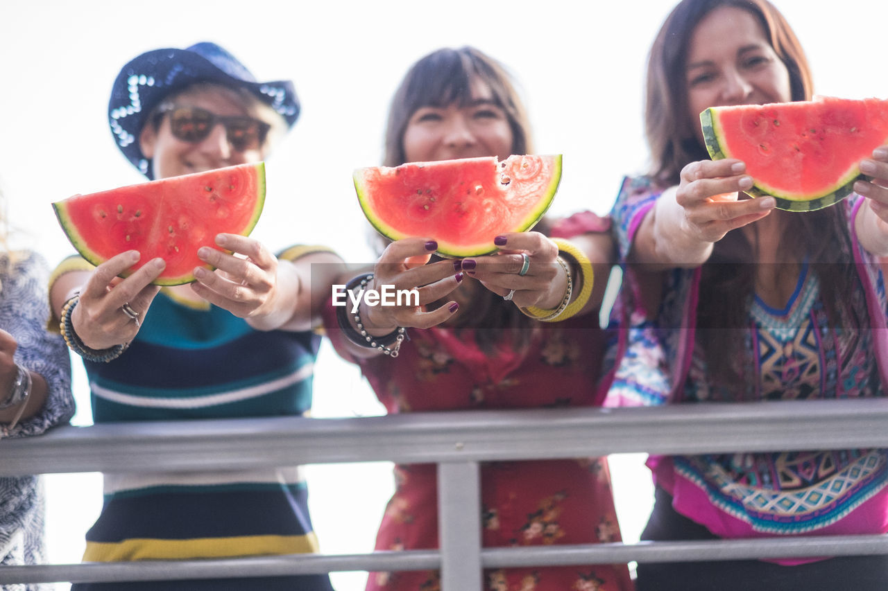 High angle view of friends holding watermelon slices while standing against sky