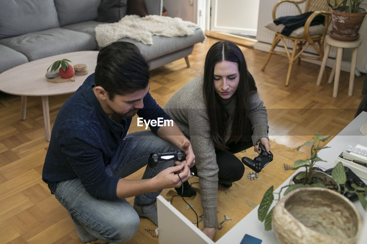 High angle view of couple removing joystick from cabinet in living room