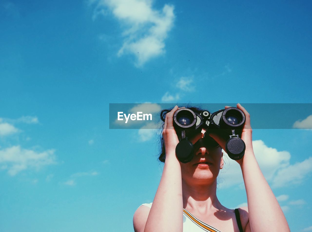 Low angle view of woman looking through binoculars against sky