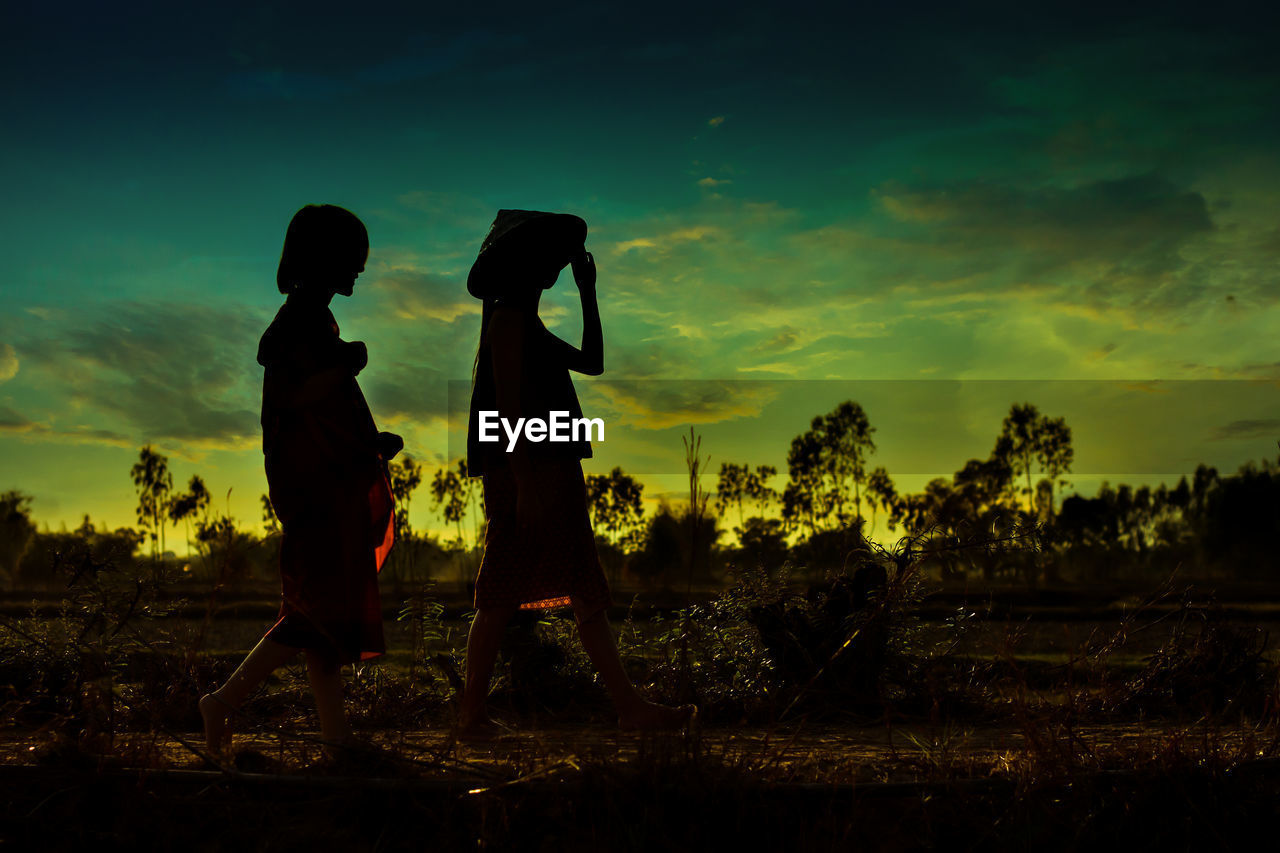 Silhouette women walking on land against sky during sunset