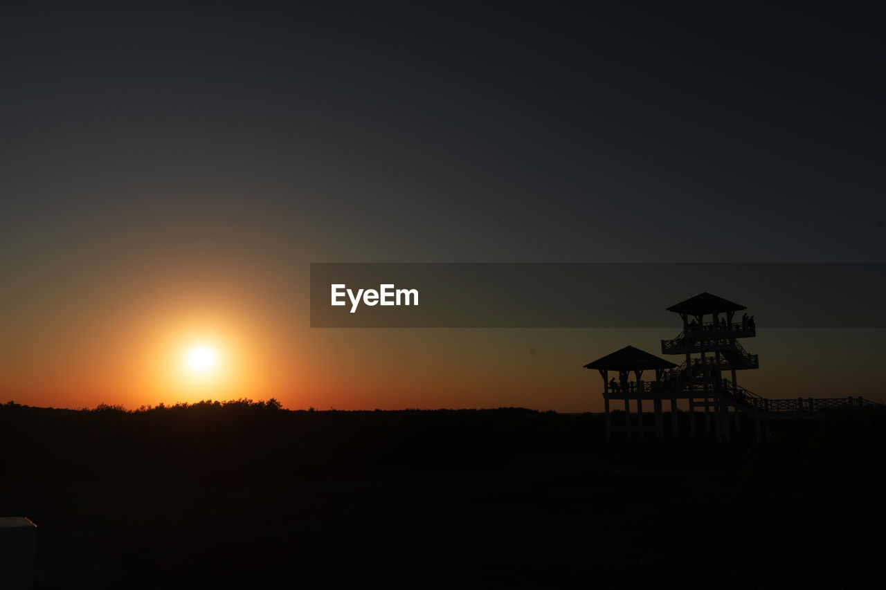 Silhouette building on shore against sky during sunset