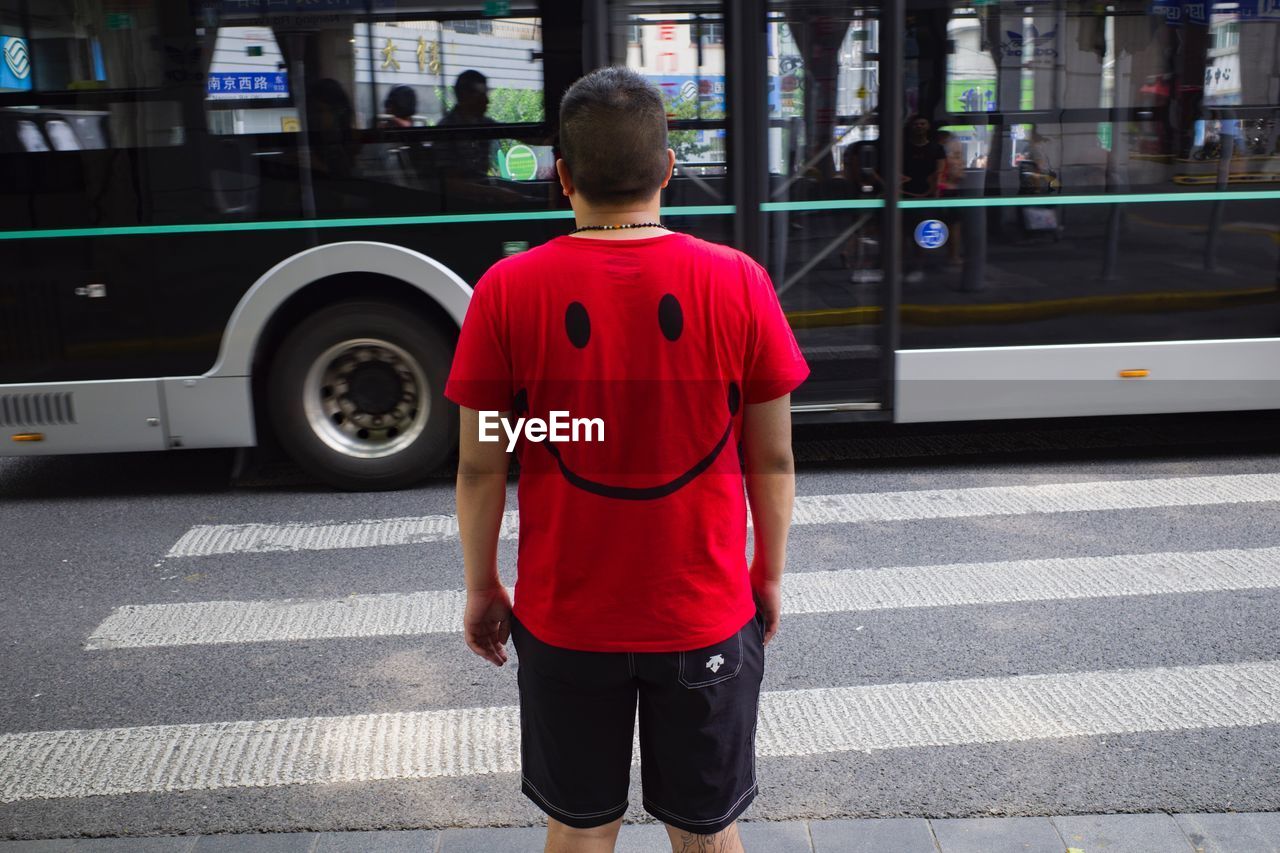 REAR VIEW OF MAN STANDING ON STREET