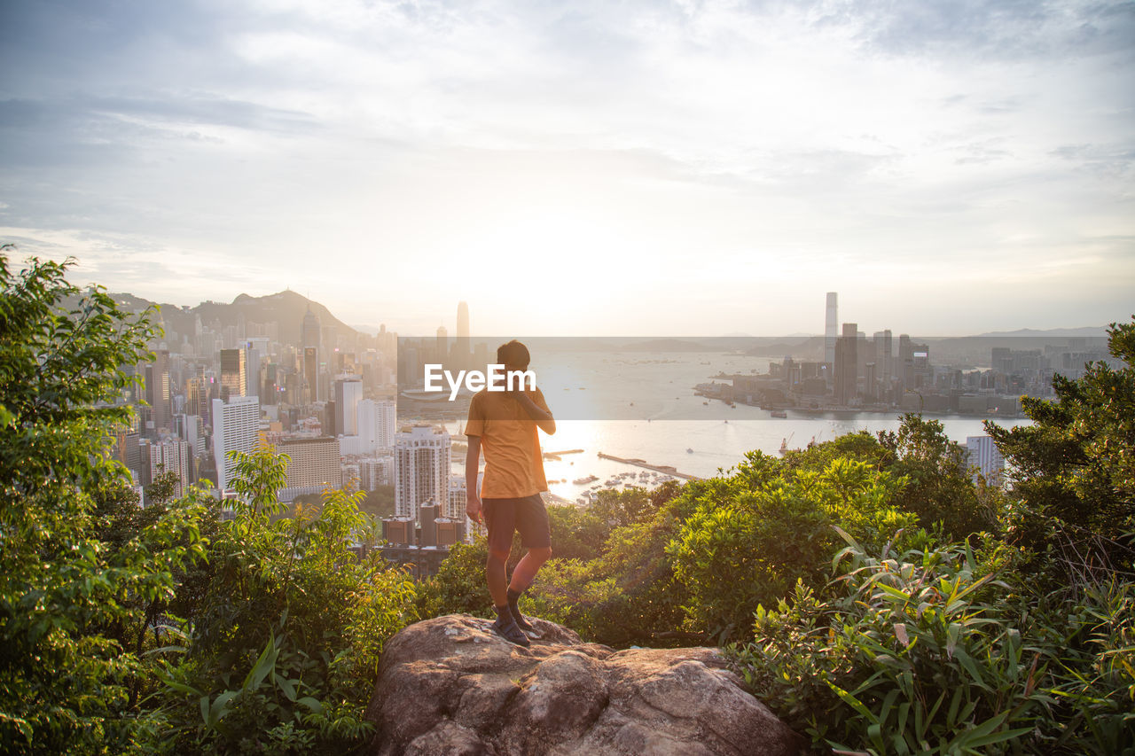 Full length of man standing on rock formation by city against sky