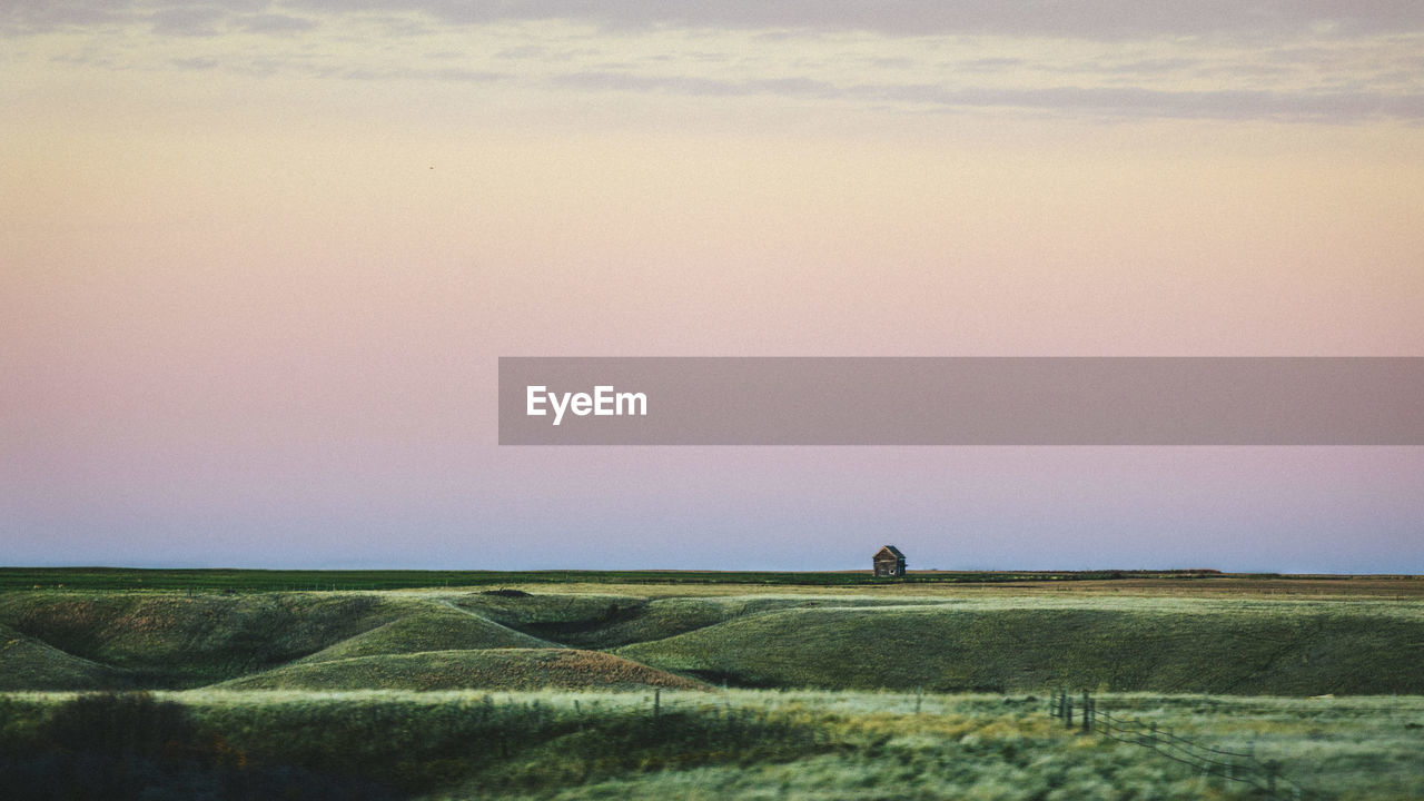 Scenic view of green landscape against sky at sunset