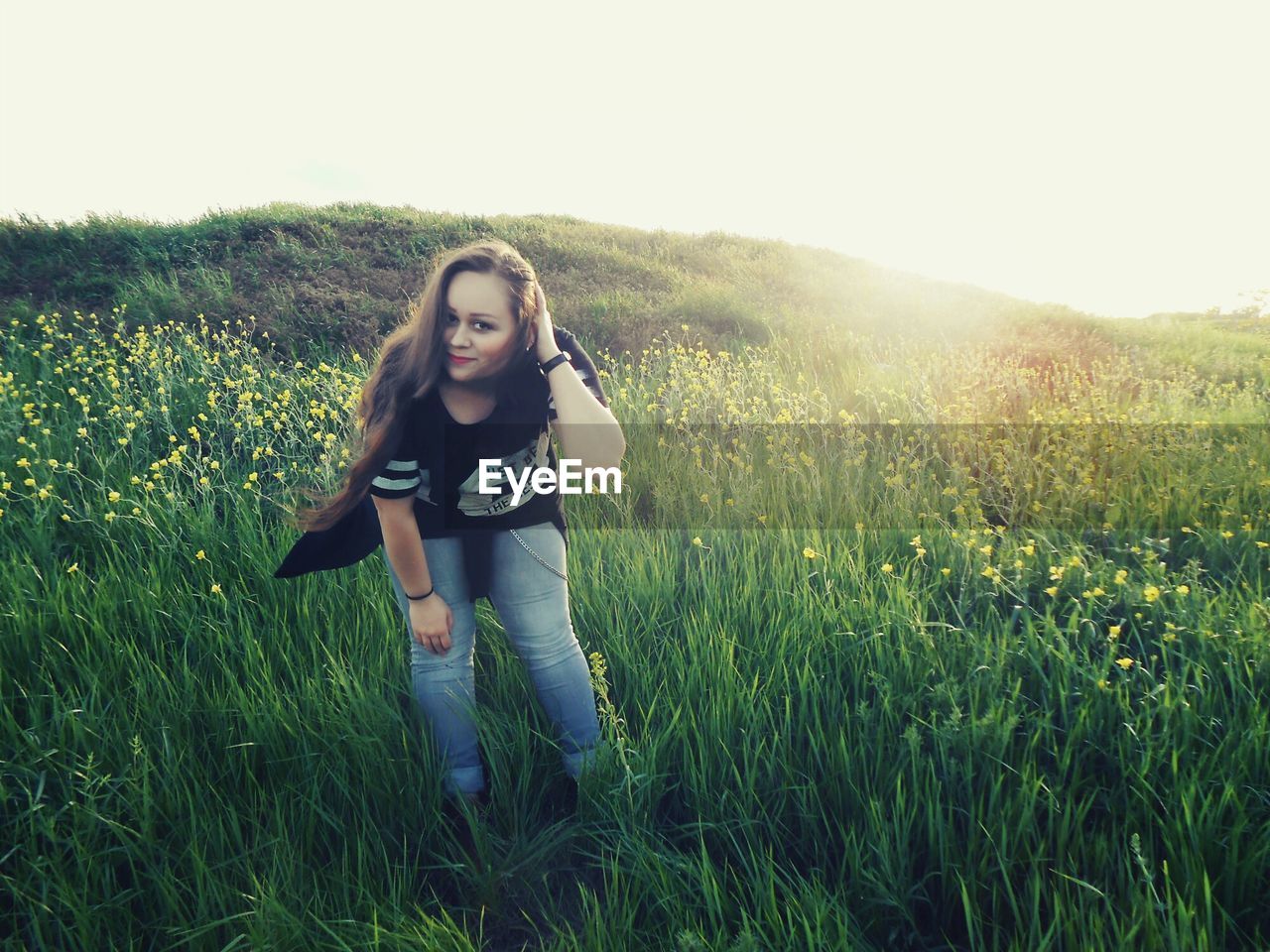 Portrait of young woman standing on grassy field against clear sky